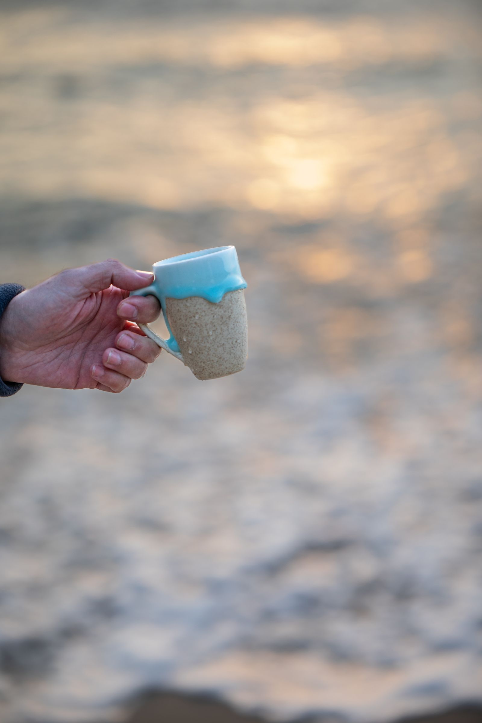 Hand mit Kaffeebecher draußen im ersten Tageslicht