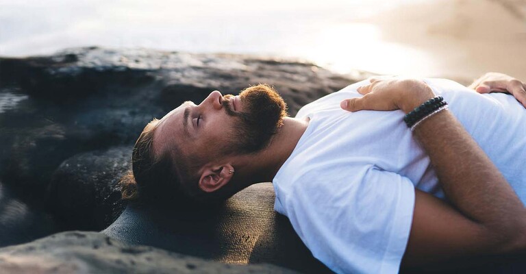 Ein Mann liegt entspannt am Strand und praktiziert Achtsamkeit